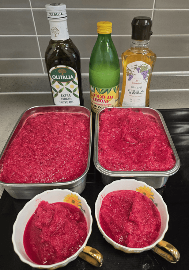 4가지 야채로 만들어진 스무디가 스테인레스 용기 및 도자기 잔 먹기 좋에 에 담겨진 모습, 그 뒤로 올리브유, 레몬즙, 알룰로스가 보인다. 